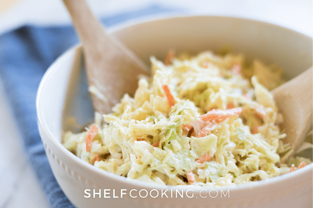 Image of a white bowl filled with leftover cabbage coleslaw and two wooden spoons. - Shelf Cooking