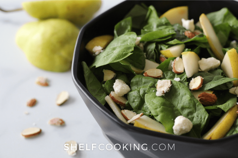 Image of a fall pear salad made with pears, almonds, spinach, and cheese in a black bowl. - Shelf Cooking