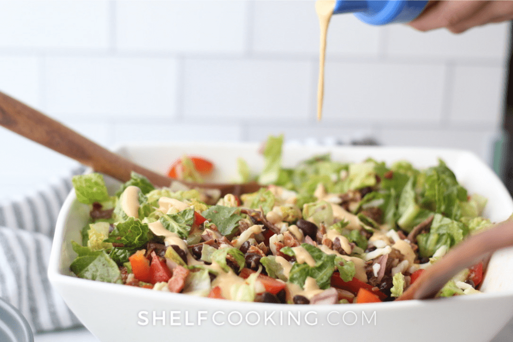 Image d'une grande salade cowboy avec de la vinaigrette versée dessus. - Cuisine d'étagère