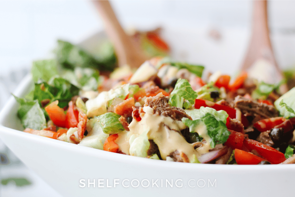 Close up image of Cowboy Salad Bowls with lettuce, tomatoes, red peppers, shredded beef, black beans, and dressing. - Shelf Cooking